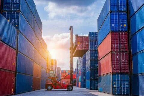Forklift lifting shipping container between stacked cargo containers