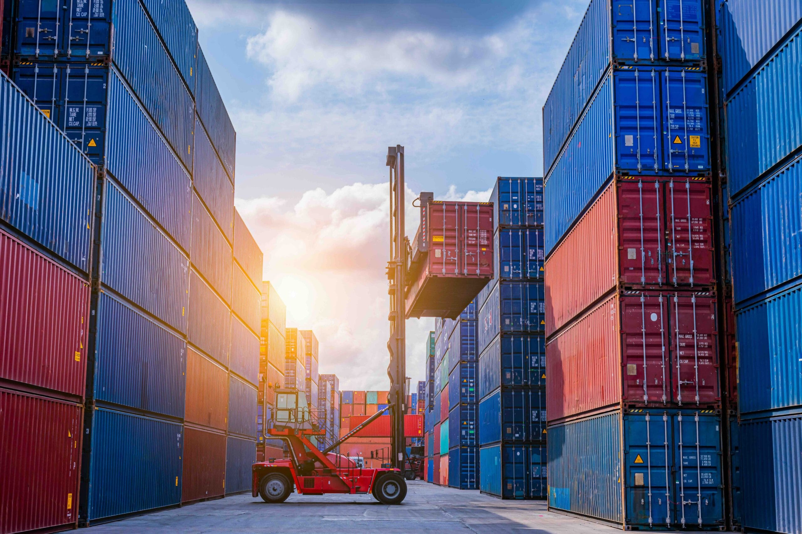 Forklift lifting shipping container between stacked cargo containers